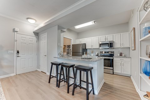 A kitchen with white cabinets and a white island with black stools.
