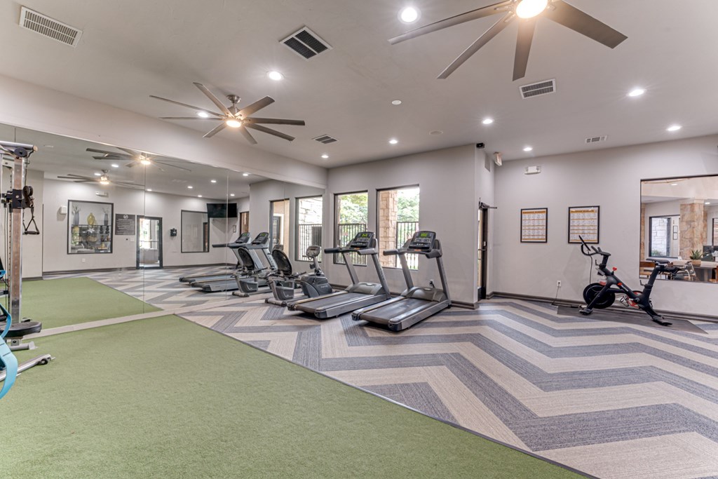 A spacious gym with a variety of equipment including treadmills, stationary bikes, and weight machines at Limestone Ranch Apartments, Lewisville