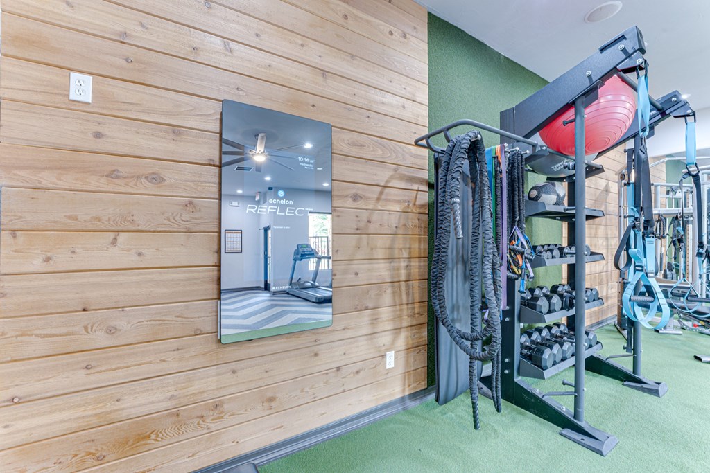 A gym with a wooden wall and a mirror reflecting a treadmill at Limestone Ranch Apartments, Lewisville