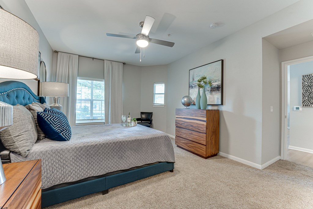 A bedroom with a bed, nightstand, and a painting on the wall at Limestone Ranch Apartments, Lewisville, Texas