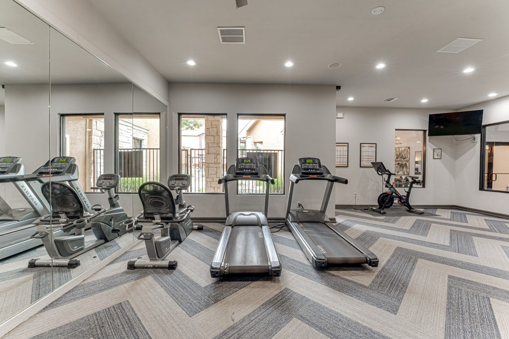 A spacious gym with treadmills, elliptical machines, and a television at Limestone Ranch Apartments, Lewisville, Texas