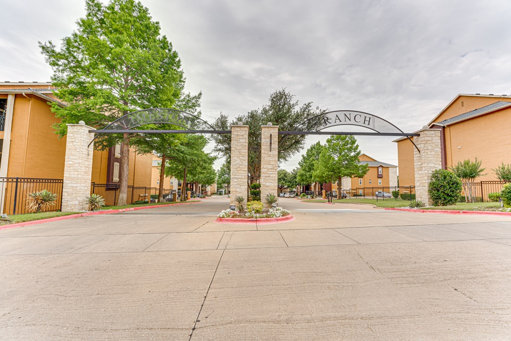 A view of a gated community entrance with a sign that reads "Ranch" at Limestone Ranch Apartments, Lewisville