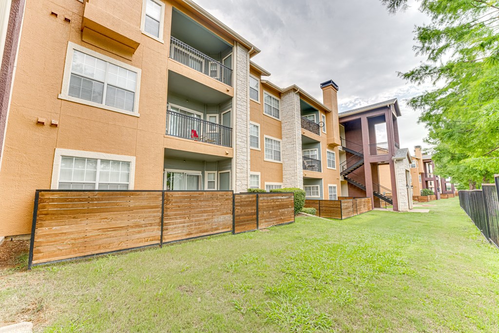 Apartment building with a brown fence and green grass in front at Limestone Ranch Apartments, Lewisville 75067