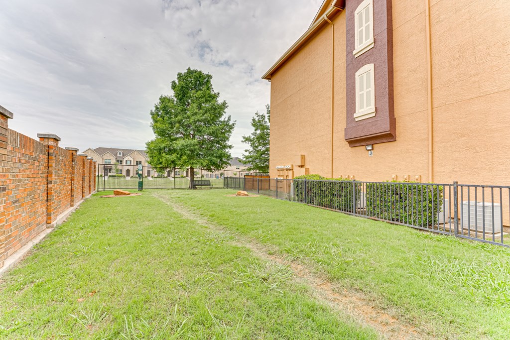 A grassy area in front of a building with a fence and a tree at Limestone Ranch Apartments, Lewisville, Texas