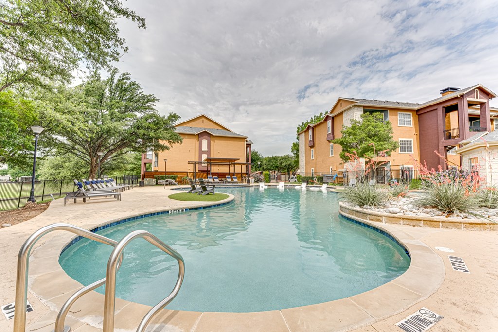 A large outdoor swimming pool surrounded by a fence and trees at Limestone Ranch Apartments, Lewisville, TX, 75067
