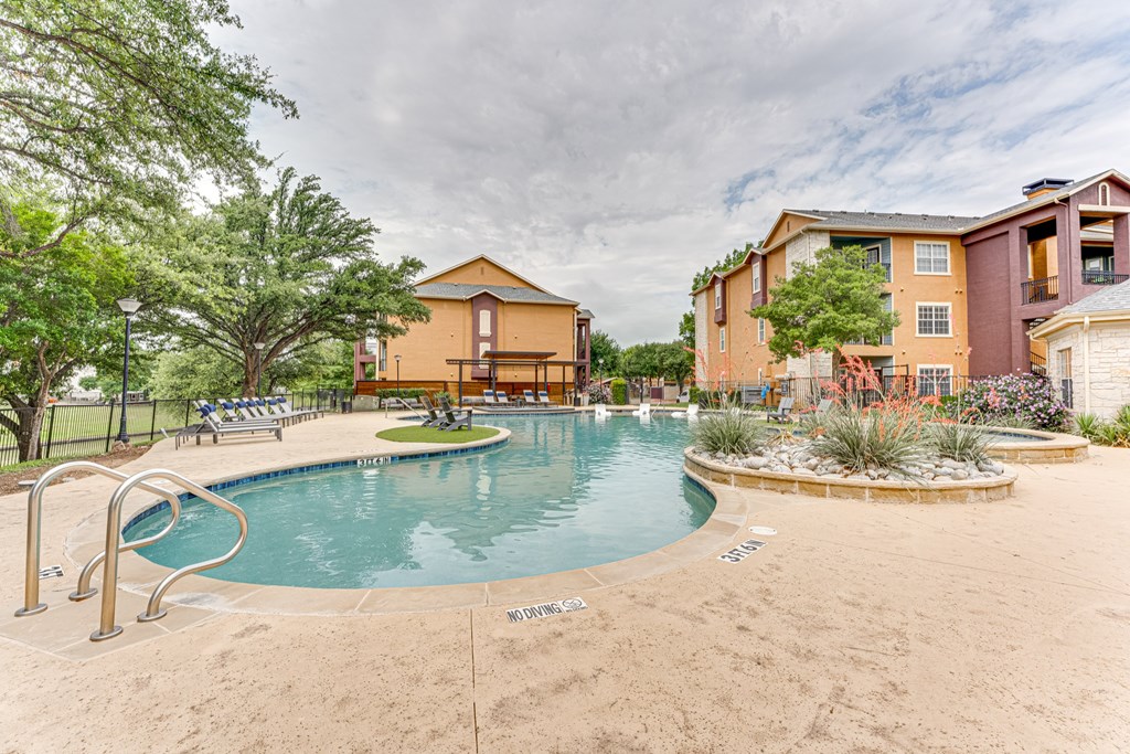 A sandy pool area with a pool and a building in the background at Limestone Ranch Apartments, Lewisville, Texas