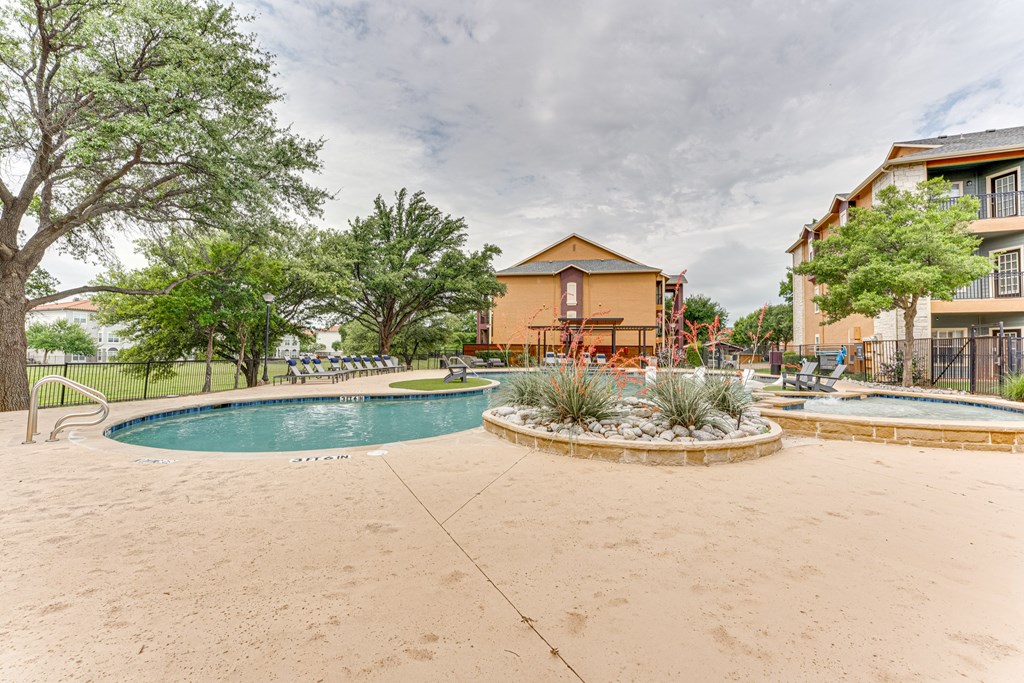 A swimming pool surrounded by a concrete patio and a small garden at Limestone Ranch Apartments, Lewisville 75067
