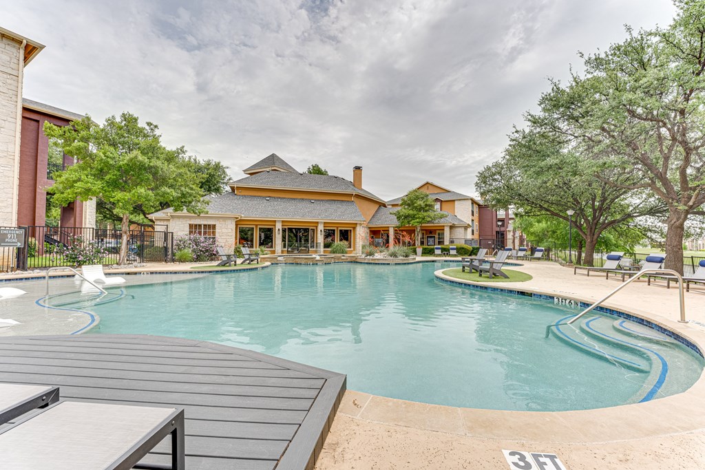 A large outdoor swimming pool with a wooden deck and a building in the background at Limestone Ranch Apartments, Texas