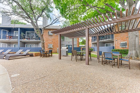 A patio with a pergola and chairs is surrounded by apartment buildings. at The Manhattan Apartments, Dallas, Texas