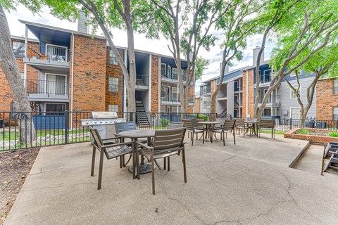 A patio with a table and chairs is surrounded by apartment buildings. at The Manhattan Apartments, Dallas