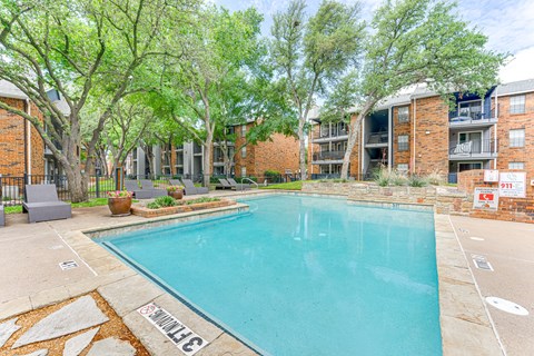 A swimming pool surrounded by trees and apartment buildings. at The Manhattan Apartments, Texas