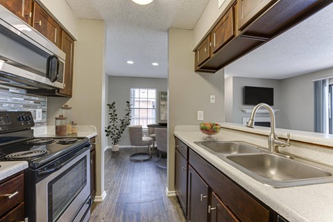 A kitchen with a black stove top oven and wooden cabinets. at The Manhattan Apartments, Dallas, 75252