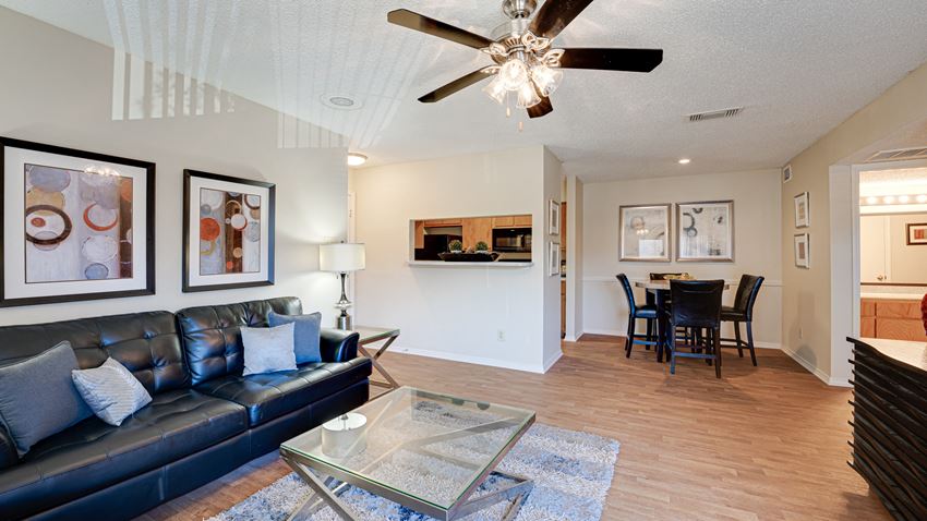 a living room with a leather couch and a glass coffee table and a dining room