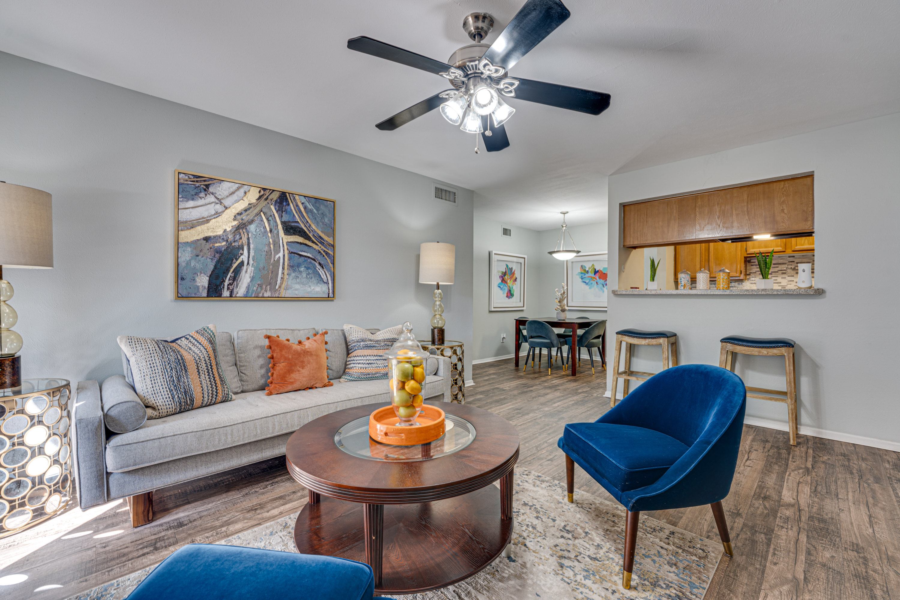 A living room with a grey couch, a blue chair, and a painting on the wall.