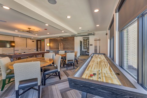 A room with a shaggy carpet and a long table with chairs and a shuffleboard table.