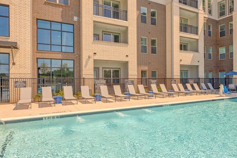 A large swimming pool in front of a building with lounge chairs around it.