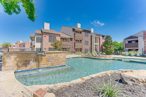 A large outdoor swimming pool surrounded by a stone wall and a grassy area.