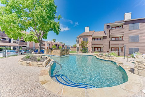 A swimming pool surrounded by a stone patio and a tree.