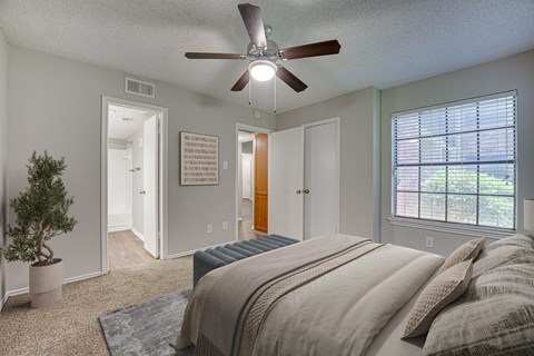 A bedroom with a bed, a ceiling fan, and a potted plant.