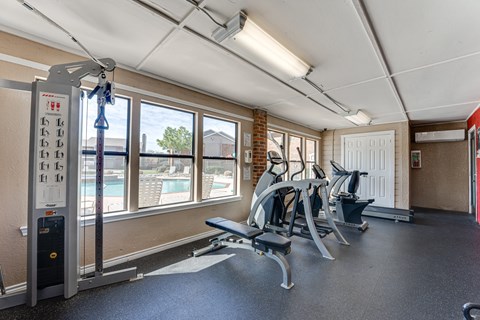 A gym with a row of exercise machines and a view of a pool outside the window.