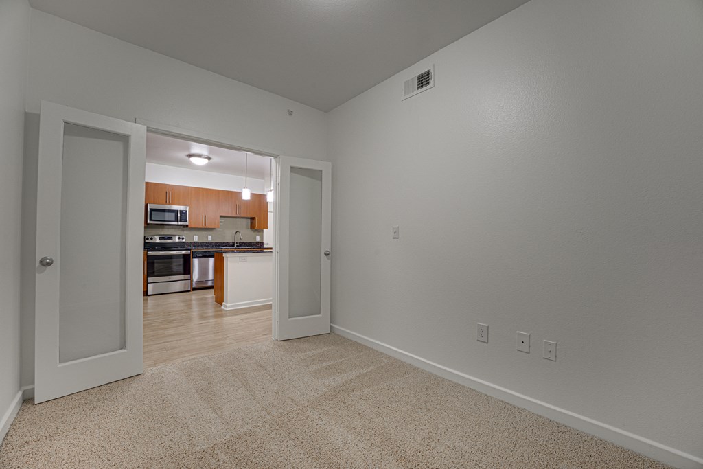 A room with a carpeted floor and a kitchen visible through the open door. at Vue Greenville, Dallas, 75206