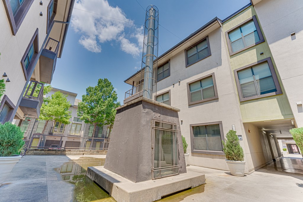 A small fountain in front of a building with a tall tower in the background. at Vue Live Oak, Dallas