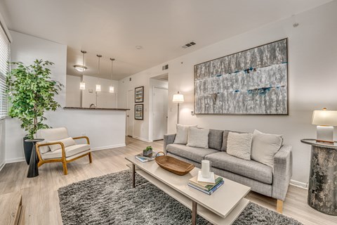 A living room with a grey couch, a wooden chair, a coffee table, and a large abstract painting on the wall.
