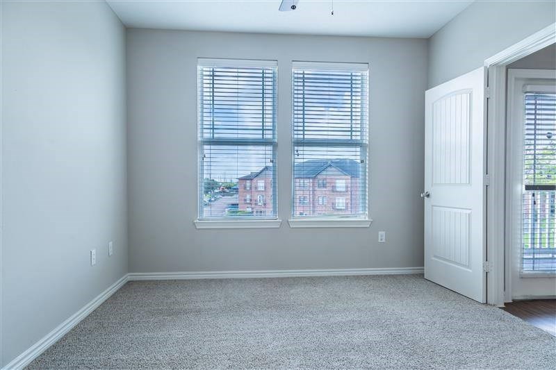 A room with a carpeted floor and a view of a house through the window.