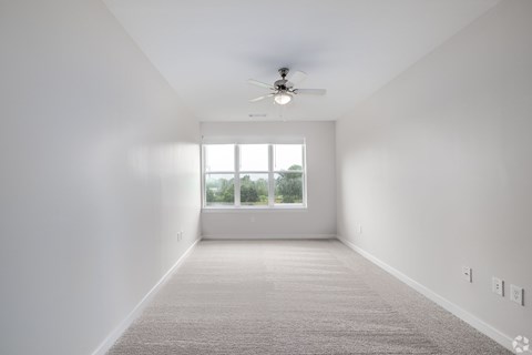 A spacious room with a ceiling fan and a large window.