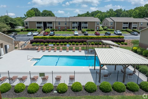 A swimming pool surrounded by a fence and bushes in front of a building.