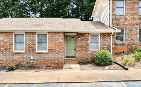 A brick house with a green door and a small bush in front.
