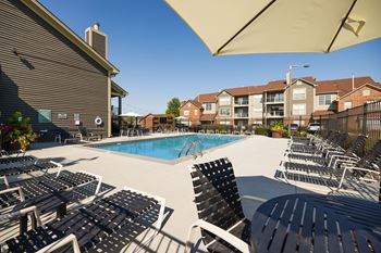 lounge chairs and an outdoor dining table poolside at Green Trails Apartments