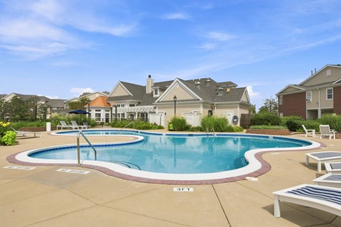 A large swimming pool surrounded by a concrete patio and lounge chairs.