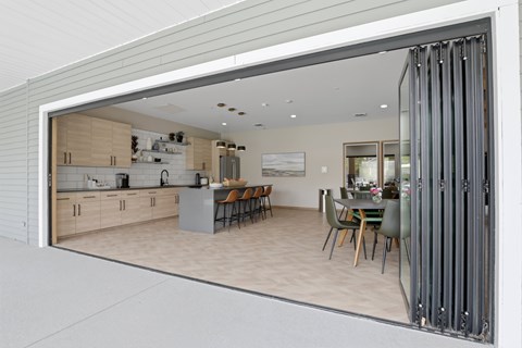 A modern kitchen with a dining table and chairs is visible through a glass door.