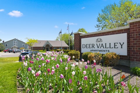 A sign for Deer Valley Apartments is in front of a building with a field of tulips.