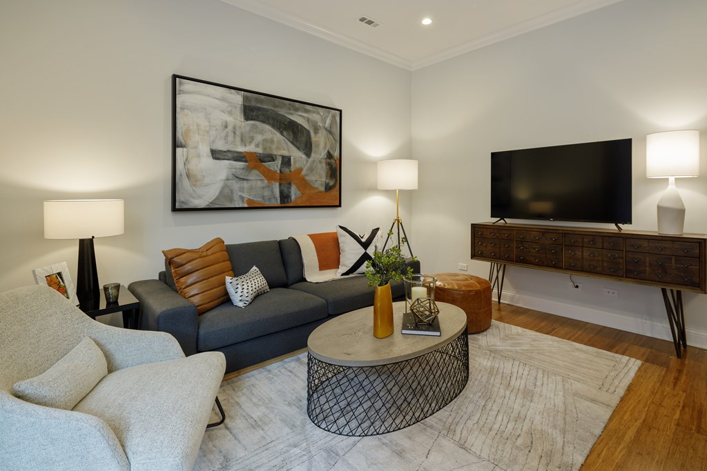 A living room with a grey couch, a round table, and a painting on the wall.
