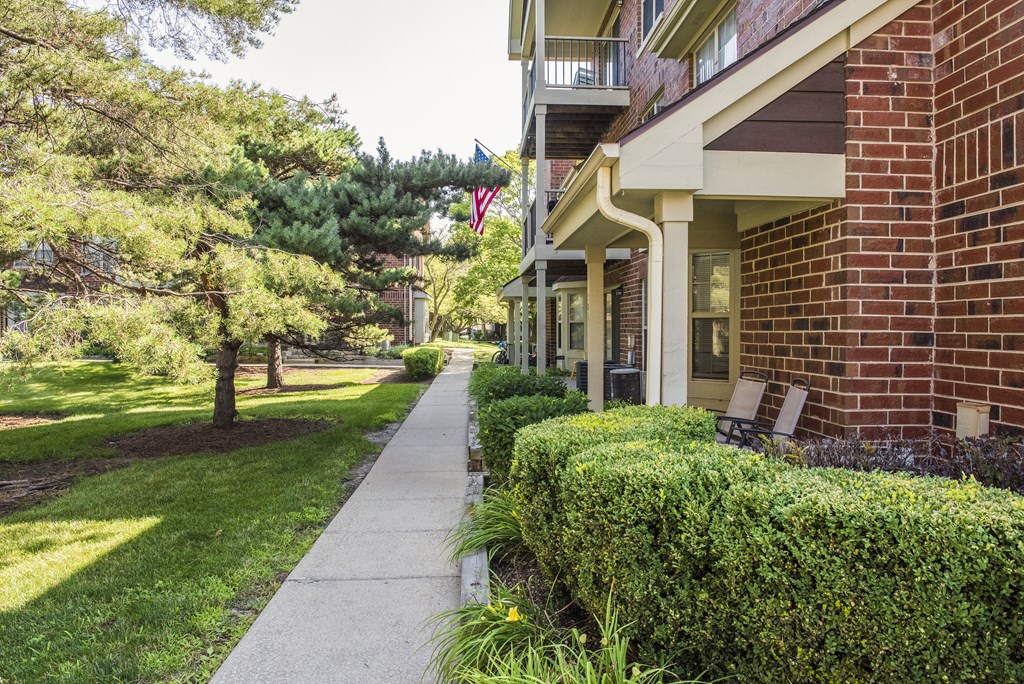 a sidewalk in front of a brick building with trees and bushes
