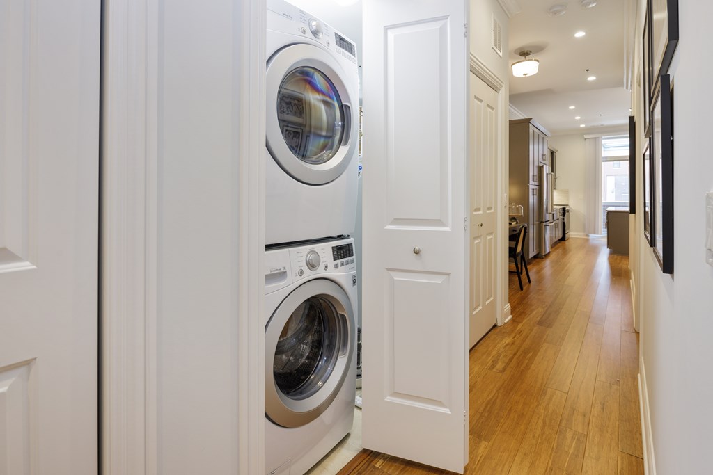 A white door is open to a hallway with a washer and dryer stacked on top of each other.