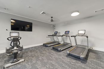 A gym room with a row of treadmills and a stationary bike.