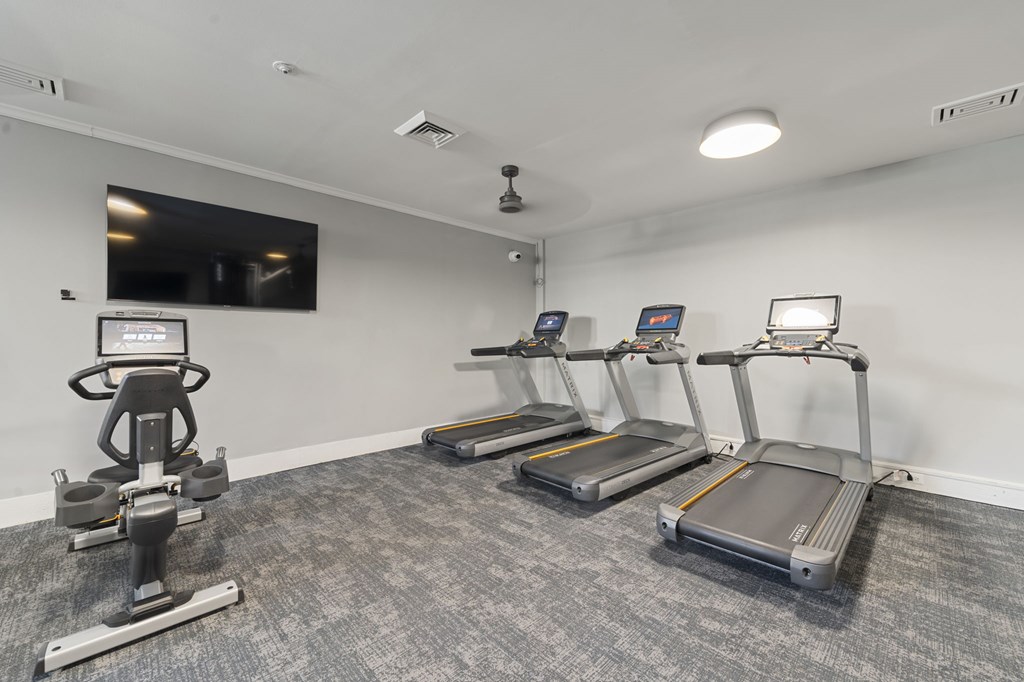 A gym room with a row of treadmills and a stationary bike.