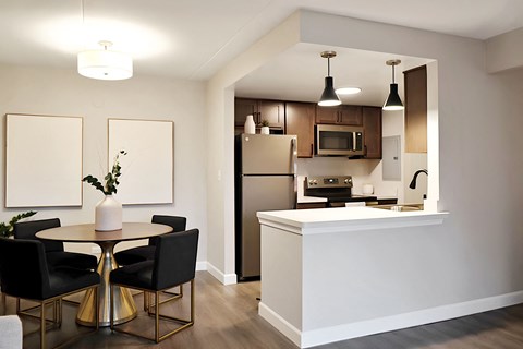 A kitchen with a table and chairs in the foreground and a refrigerator, microwave, and oven in the background.