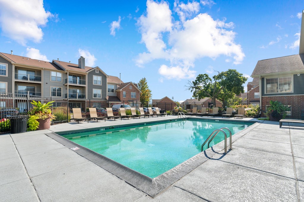 A swimming pool surrounded by lounge chairs and buildings in the background.