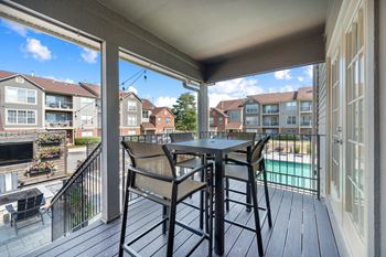 A patio with a table and chairs overlooks a pool and apartment buildings.