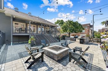 A patio with a table and chairs is surrounded by a brick building and a tree.