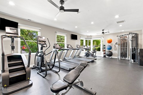 A spacious gym with treadmills, elliptical machines, and a fan.