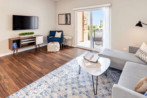 A living room with a grey couch, a blue chair, a white coffee table, and a wooden cabinet with a flat screen TV mounted above it.