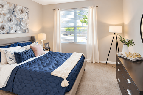 A bedroom with a large bed and a window with white curtains.