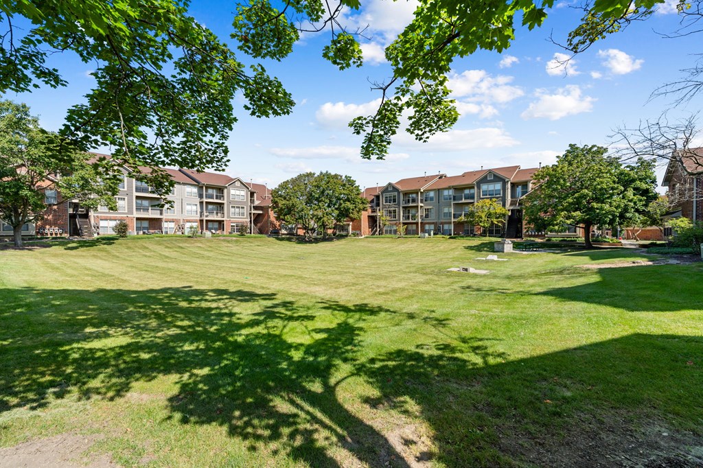 A grassy area with trees and apartment buildings in the background.