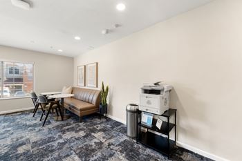 A room with a couch, a printer, and a trash can.