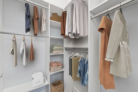 A white closet with clothes hanging and shelves.